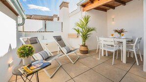 A modern outdoor patio with a dining area, lounge chairs, and potted plants. - Debambú Suites (Málaga)