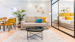 A modern living room with a sofa, coffee table, and dining area. - Debambú Suites (Málaga)