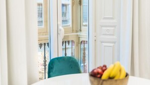 A view through a window with a white door, a green chair, and a bowl of fruit on a table. - Debambú Suites (Málaga)