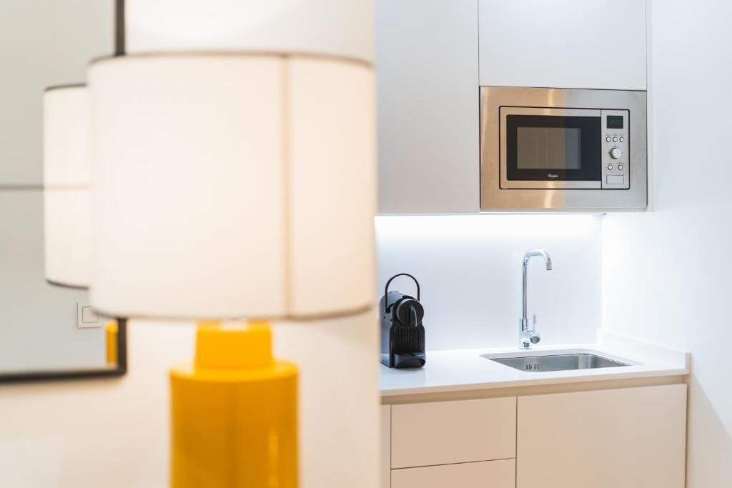 Une cuisine moderne équipée d’un four à micro-ondes encastré, d’un évier et d’une lampe jaune.
