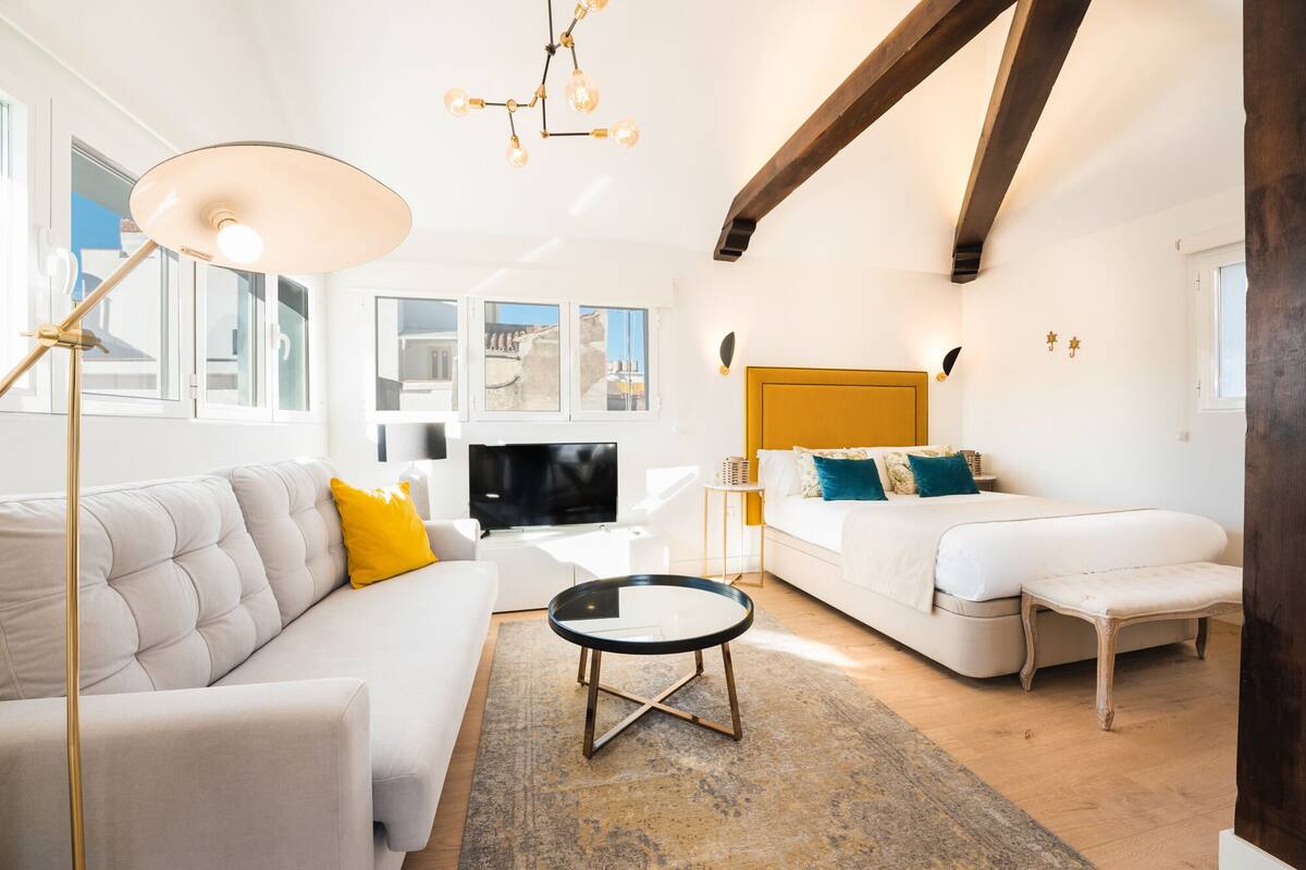 Uma sala de estar moderna com sofá, mesa de centro, televisão e cama com cabeceira de madeira.