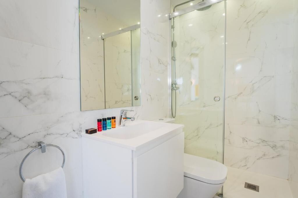 Un baño moderno con lavamanos de mármol blanco, ducha envuelta en vidrio y un inodoro.