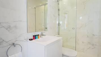 Un baño moderno con lavamanos de mármol blanco, ducha envuelta en vidrio y un inodoro.