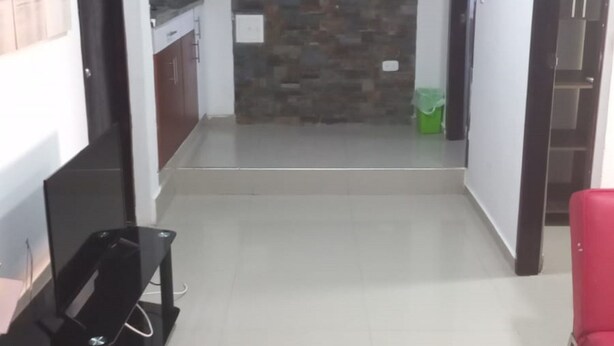 Un pasillo con pared de piedra, una zona de cocina con armarios y una silla roja.