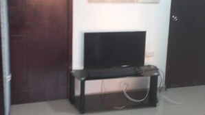 Una sala de estar con televisor de pantalla plana sobre un mueble, un sofá rojo, una puerta y un cuadro colgado en la pared.