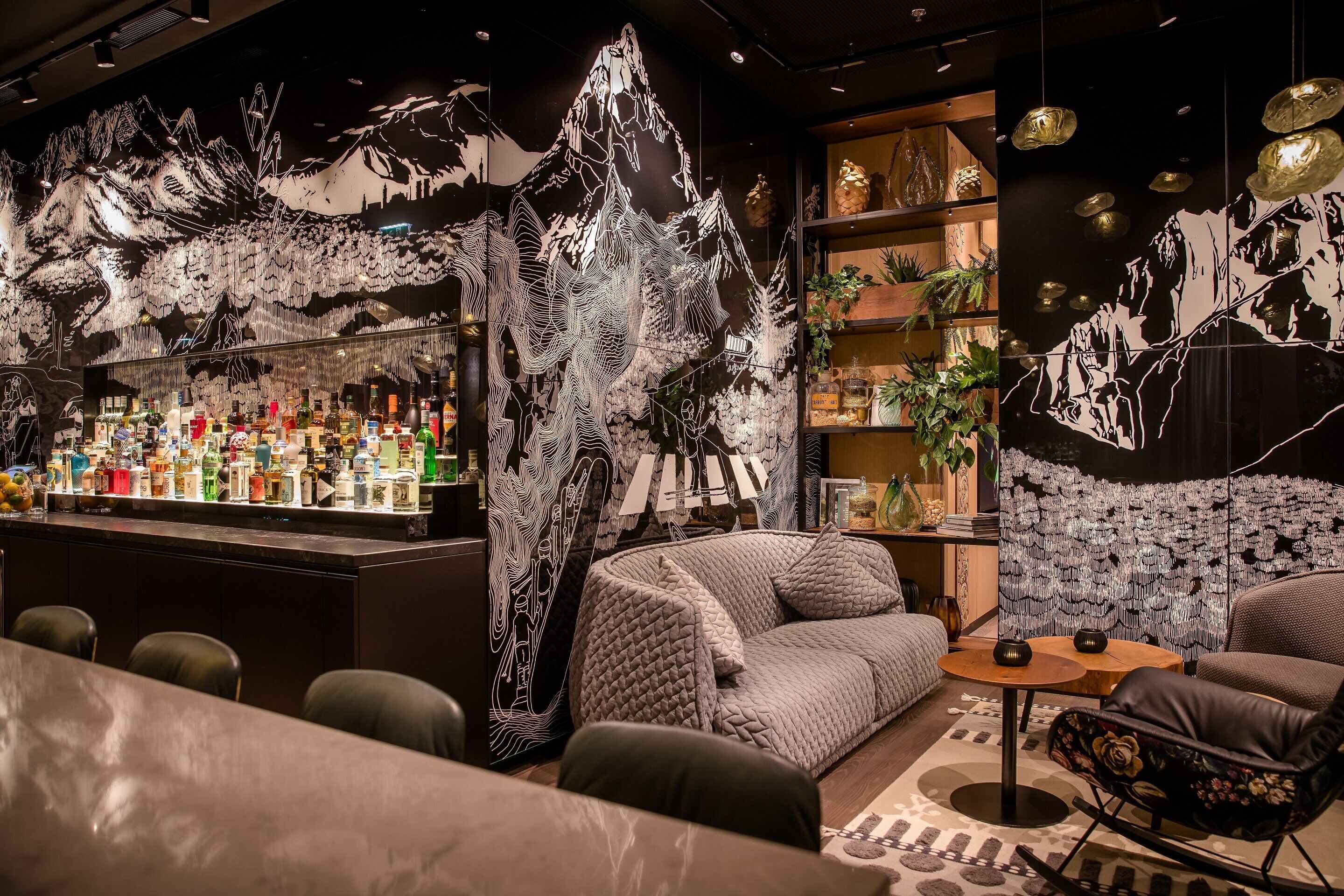 A bar area with a variety of bottles, a seating area with a sofa and chairs, and a wall with a mountain design.