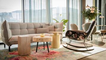 A modern living room with a beige sectional sofa, a wooden coffee table, a rocking chair, and a colorful rug.