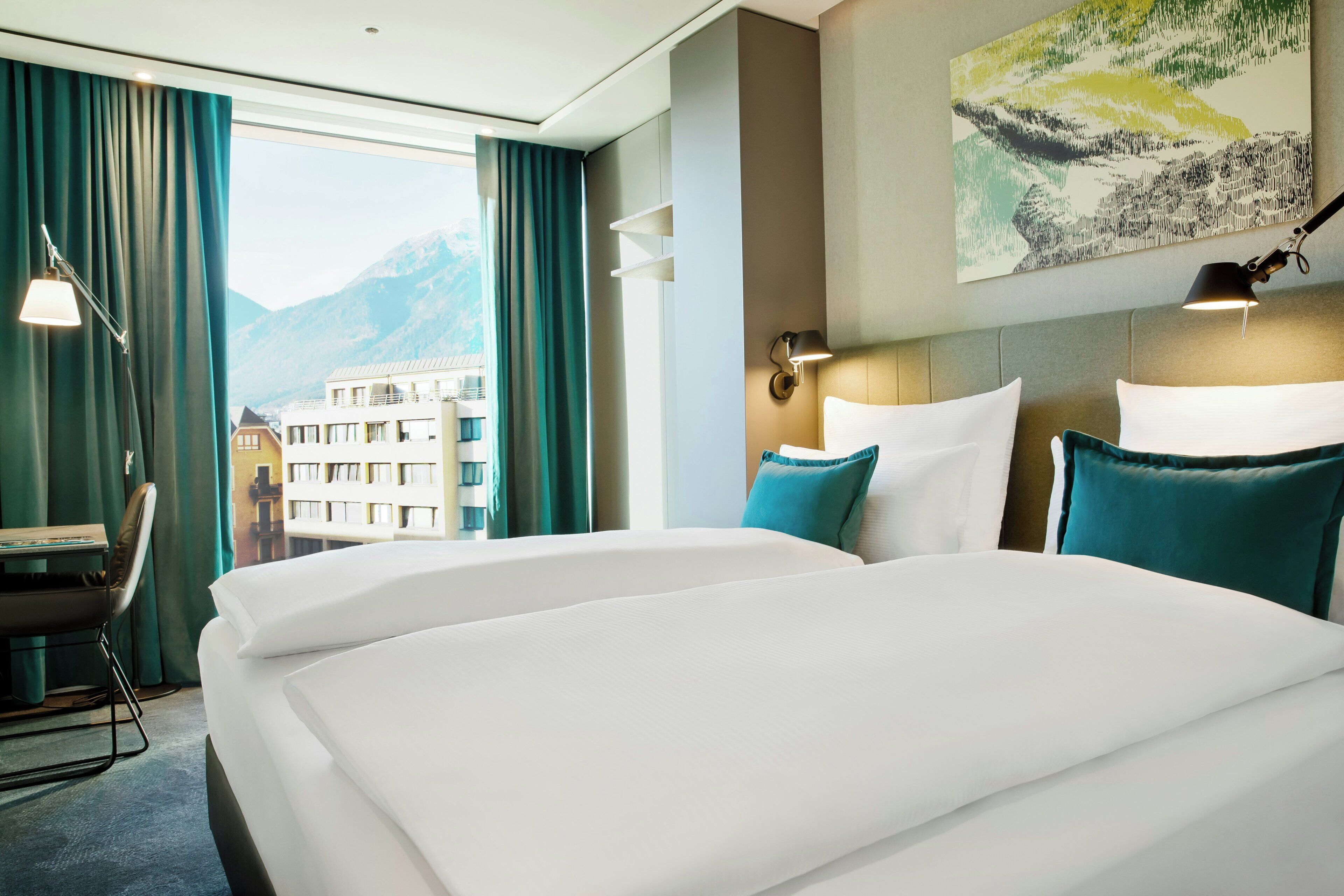 A hotel room with a large bed, a desk, and a view of mountains.