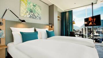 A hotel room with a large bed, a flat-screen TV, a city view, and a painting on the wall.