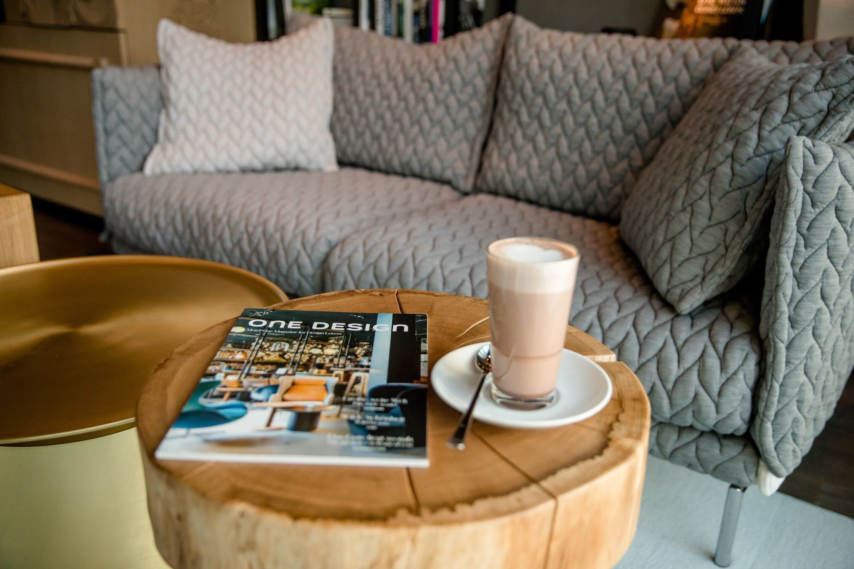 Un magazine intitulé « ONE DESIGN » est posé sur une table en bois, à côté d’une tasse de café.