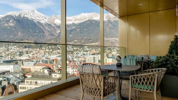 Ein Balkon mit Blick auf eine Stadt und Berge. Korbstühle und ein Tisch mit einer Vase sind vorhanden.