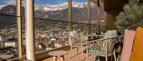 A balcony with wicker furniture, a small table, and a view of a town and mountains.