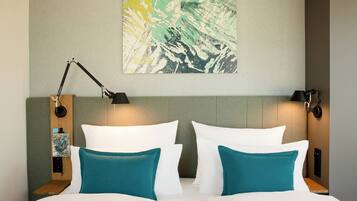 Een netjes opgemaakt bed met witte en teal kussens, een hoofdbord met een bevestigd abstract schilderij, en twee nachtlampjes.