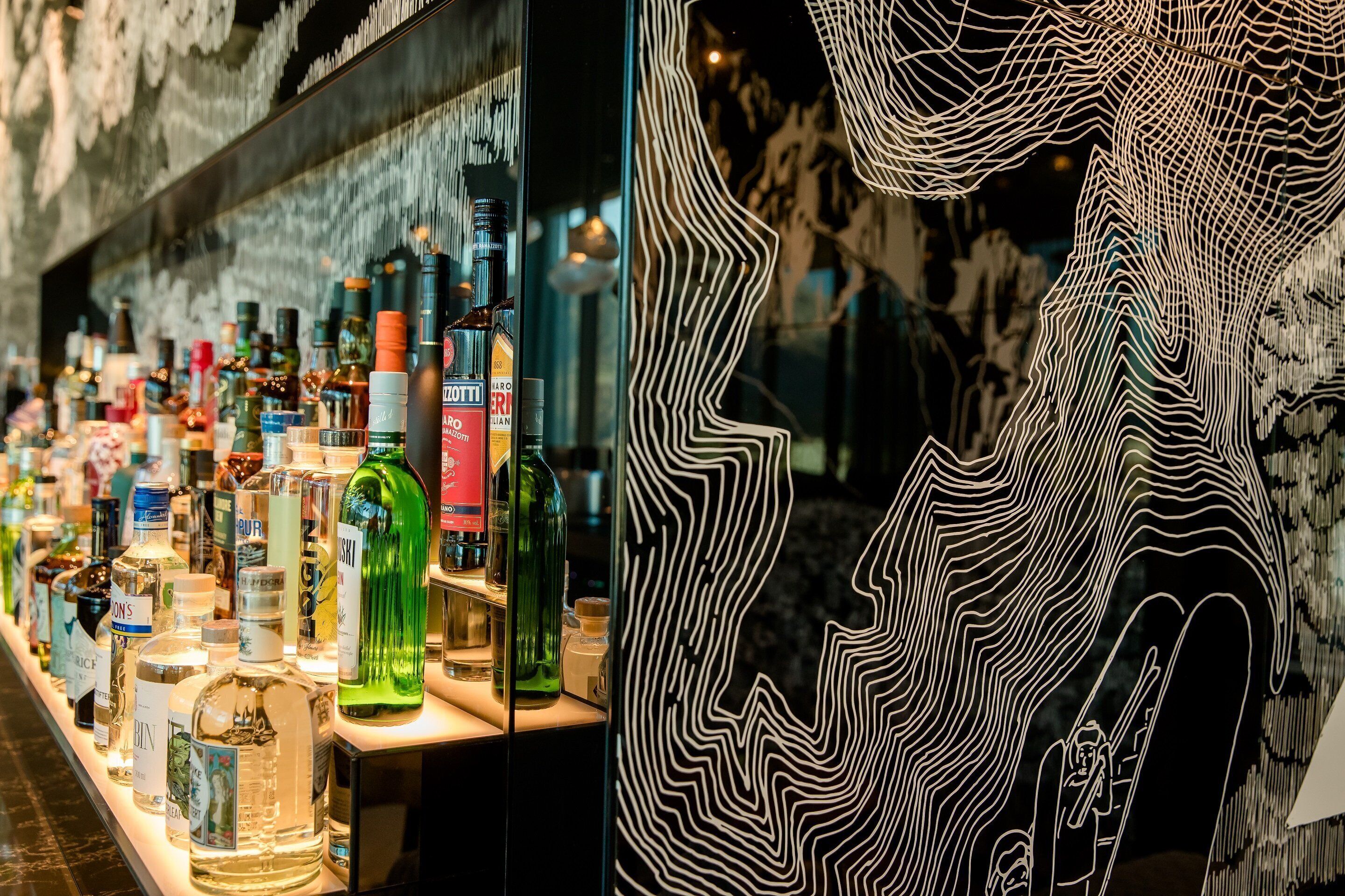 A bar with various liquor bottles and a large abstract wall art piece.