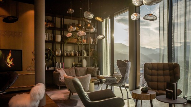 A modern living room with a fireplace, comfortable seating, a bookshelf, and a view of mountains through large windows. - Motel One Innsbruck (Innsbruck)