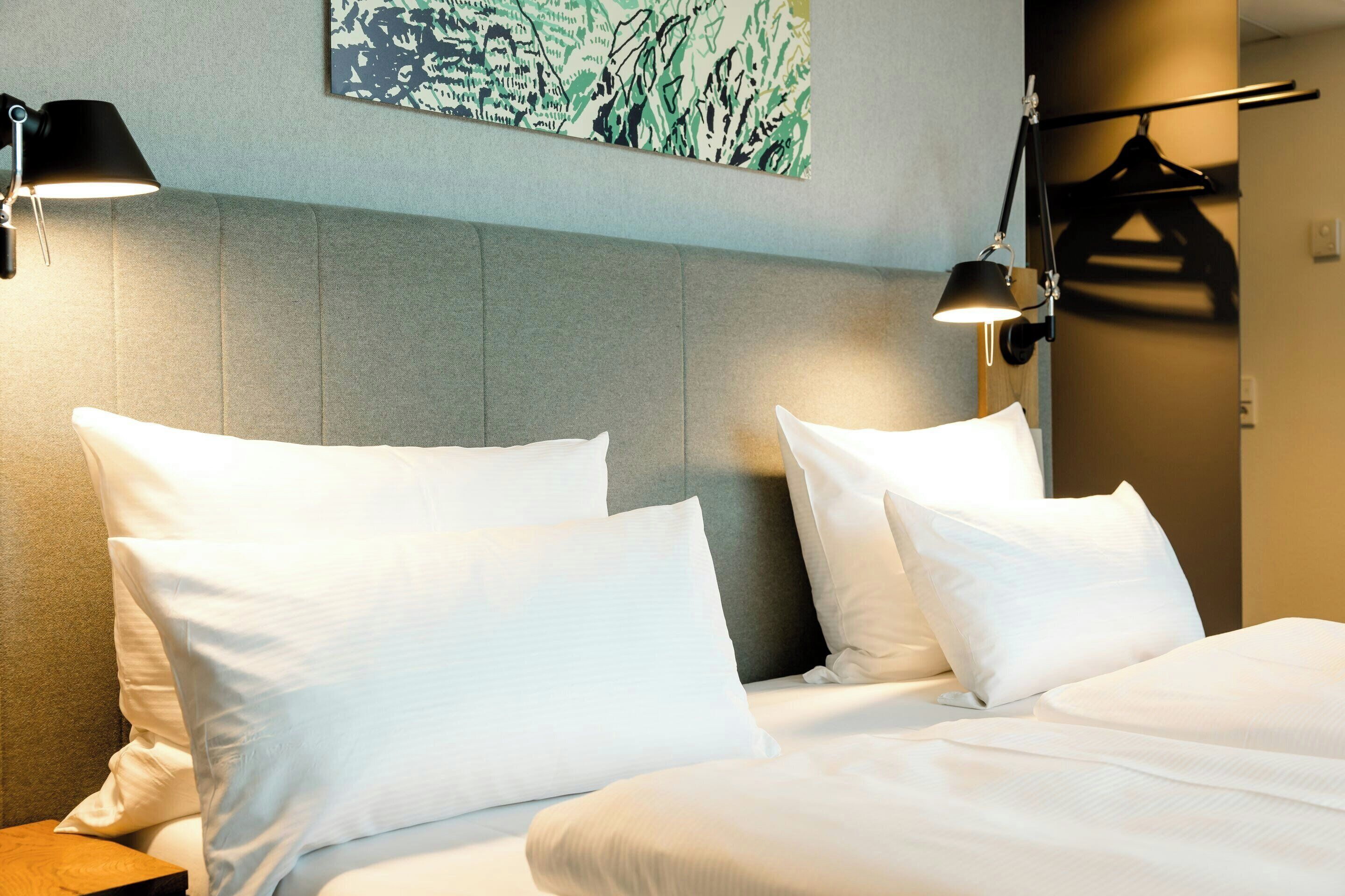 A hotel room with a bed, two bedside lamps, and a wall-mounted artwork.