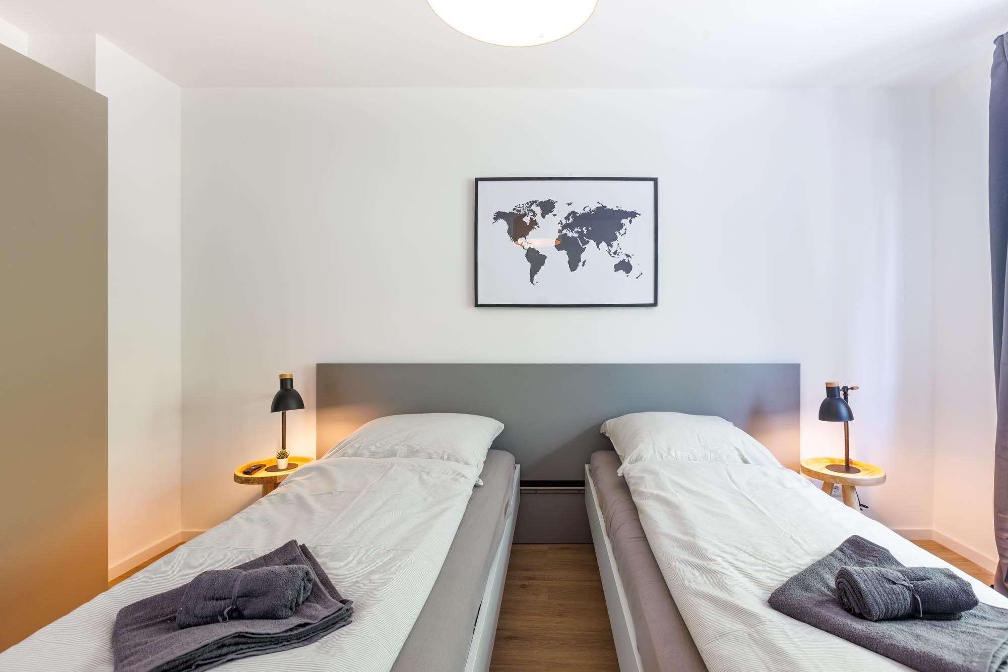 Ein Doppelzimmer mit zwei Betten, einer Weltkarte an der Wand und Nachttischlampen.