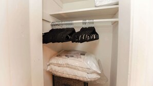 Ein Schrank mit einem weißen Regal, einer Kleiderstange mit schwarzen Kleiderbügeln und einem Stapel weißer Kissen.