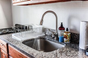 A kitchen with a granite countertop, stainless steel sink, and a dish rack.