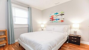 Ein ordentlich eingerichtetes Schlafzimmer mit einem Bett, Nachttischlampen, einem Holznachttisch und einem Fenster mit Vorhängen.