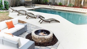 Ein Garten mit Pool, Liegestühlen, Feuerstelle und Grillhaus.