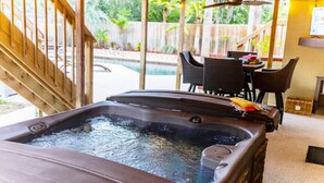 Ein Whirlpool mit Holzterrasse und Schwimmbad im Hintergrund.