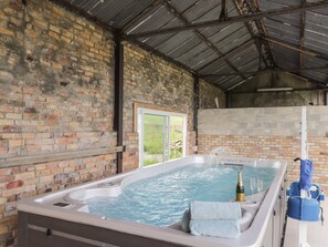 A hot tub with water jets, a bottle of champagne, and two glasses, set against a brick wall with a metal roof. - Moss of Bourach (Aberlour)