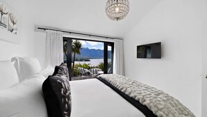 Une chambre moderne dotée d’un grand lit, offrant une vue sur les montagnes et l’eau, d’un lustre et d’un téléviseur à écran plat.