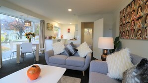 A modern living room with a grey sofa, white armchairs, and a white coffee table. There is a kitchen area with a dining table and chairs visible through an open door. - CENTRAL CITY APARTMENT, FREE PARKING, BAY VIEWS (Queenstown)