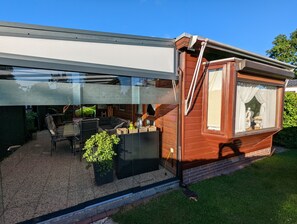 Ein modernes Haus mit Glaserker, Sitzgelegenheiten im Freien und einem kleinen Garten.