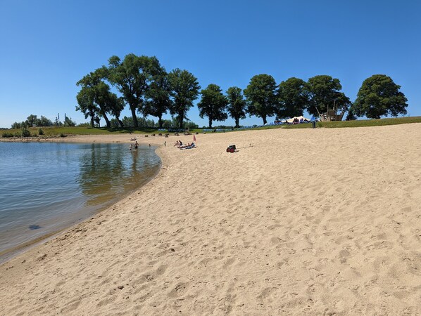 Ein sandiger Strand mit einem ruhigen See, Bäumen und einigen Personen.