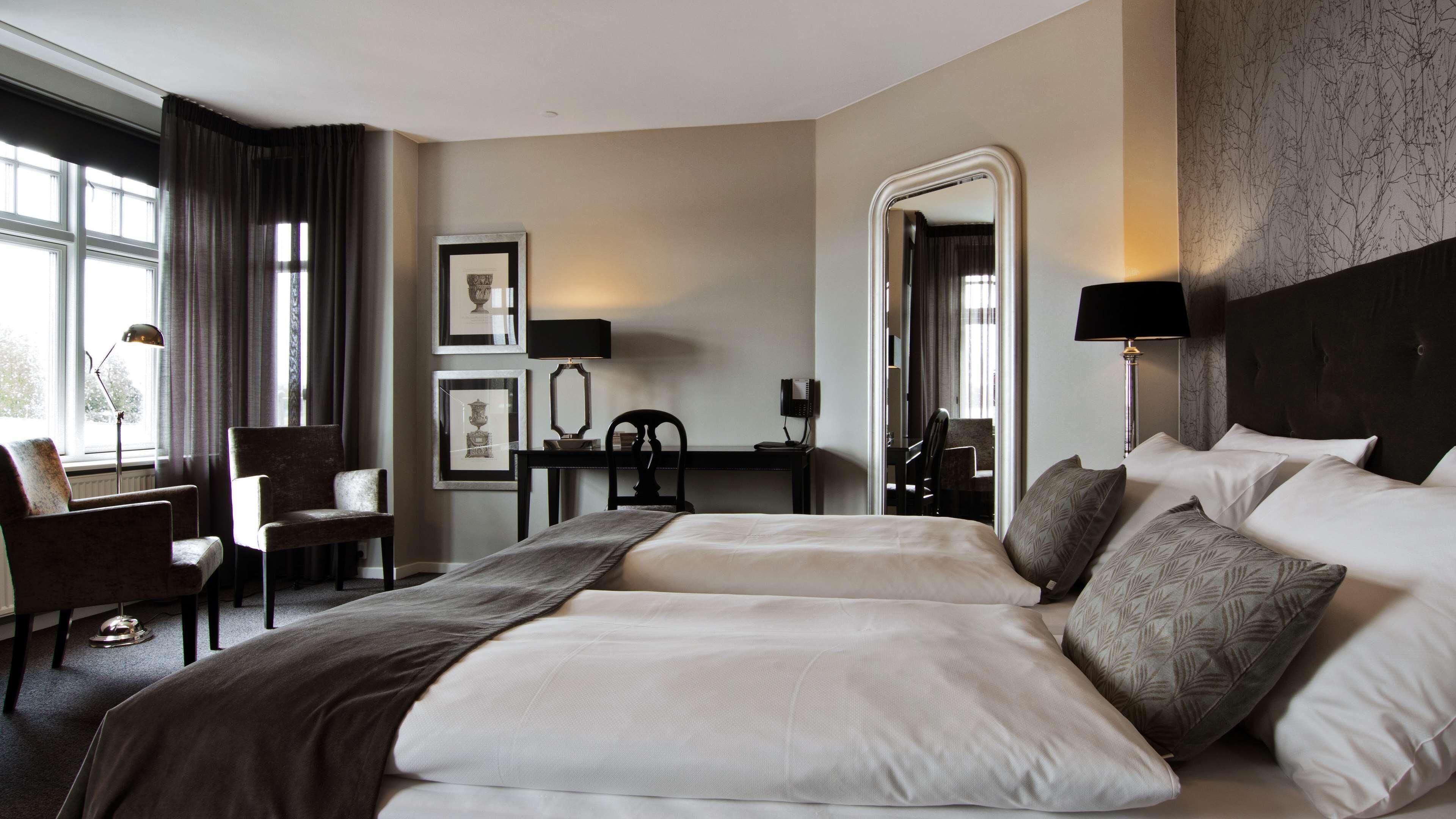 A hotel room with a large bed, a desk, a chair, a mirror, and a view of the outdoors.
