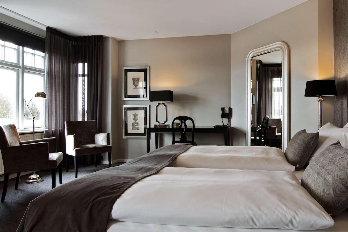A hotel room with two beds, a desk with a chair, a large mirror, and artwork on the wall.