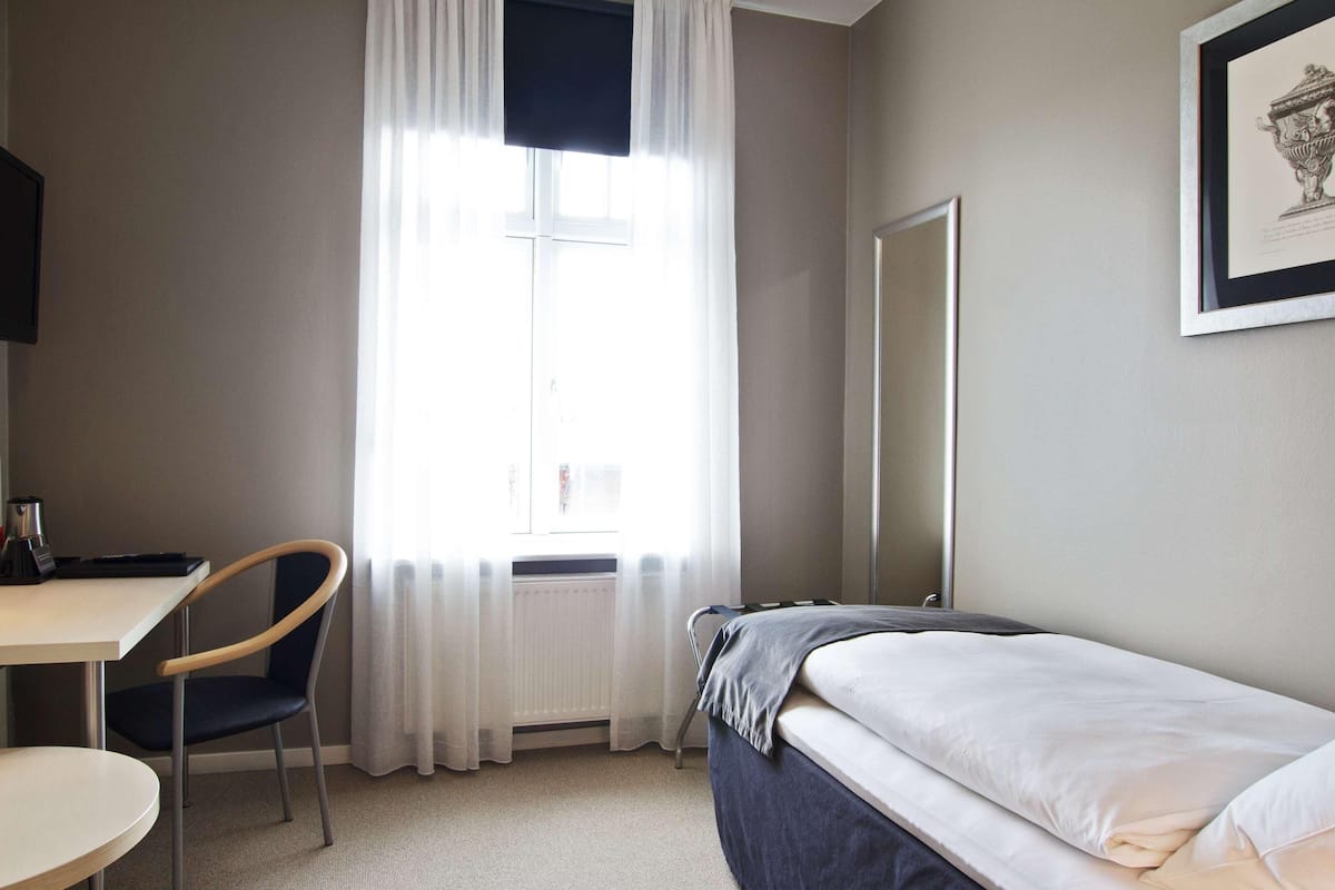 A hotel room with a bed, a desk, a chair, a TV, and a window with curtains.