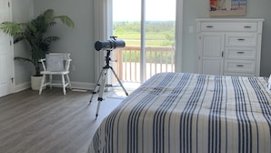 Una camera da letto con un letto, una ventola a soffitto, una pianta in vaso, un treppiede con una macchina fotografica e un balcone vista esterna.