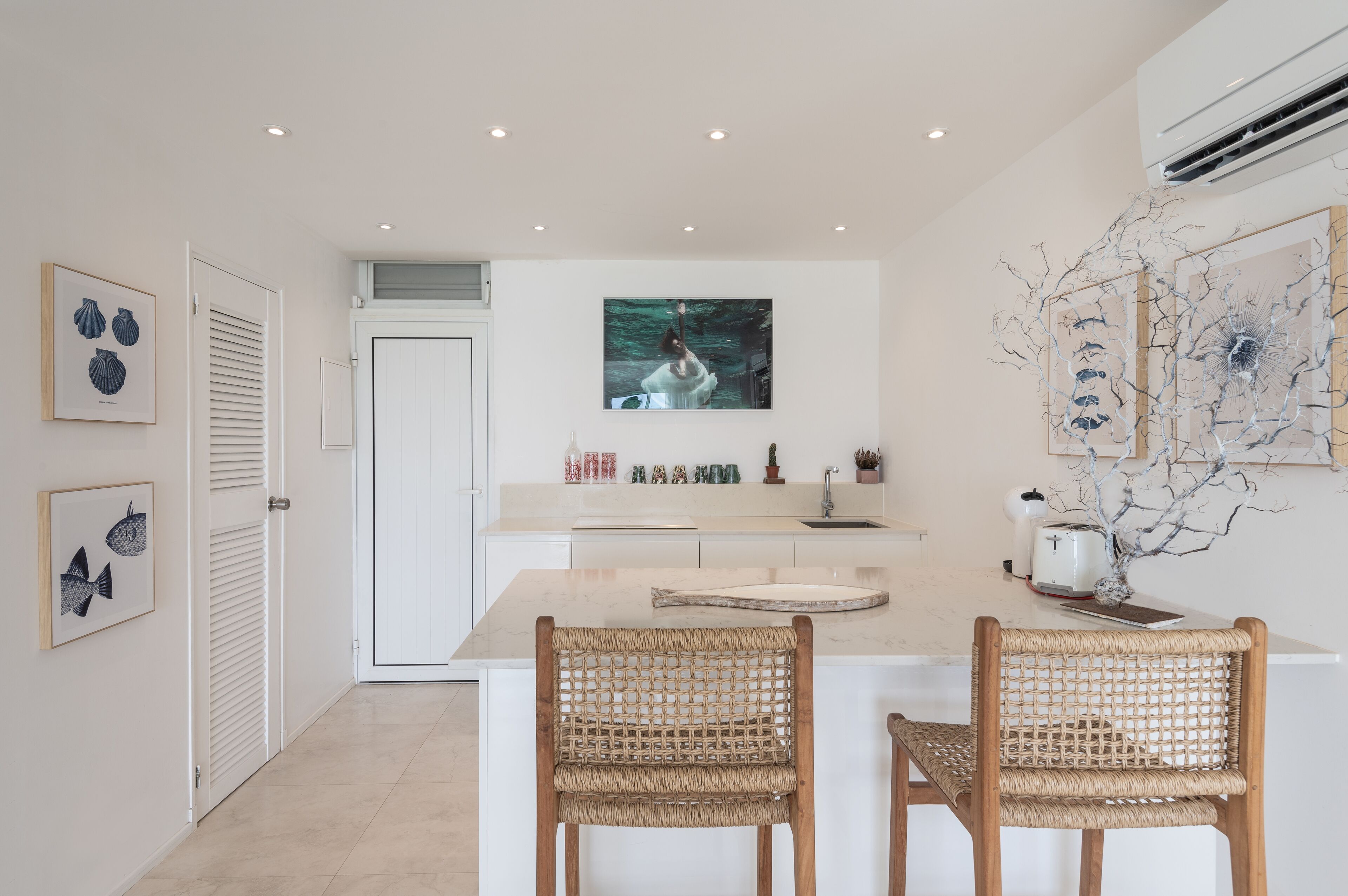 A modern kitchen with white cabinetry, a central island, and two wicker chairs.