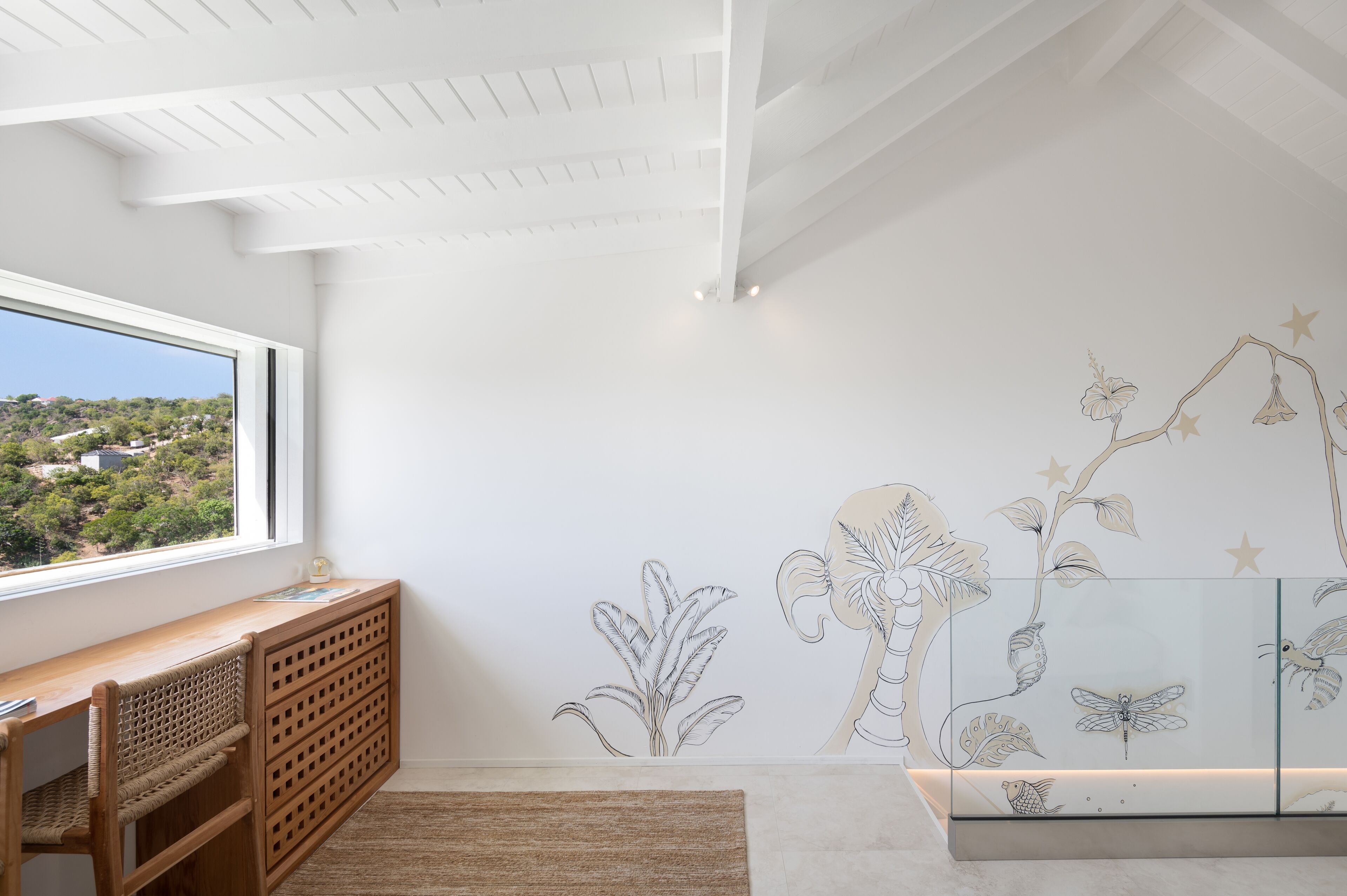 A room with a large window, a wooden desk, a radiator, and a wall mural with nature illustrations.