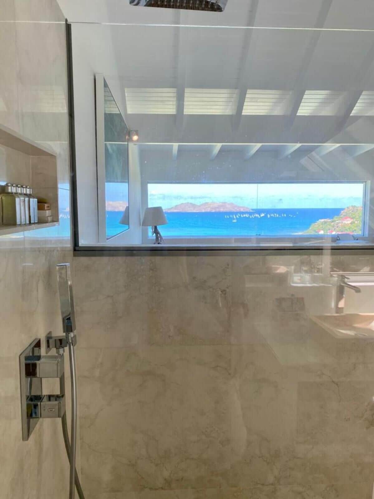 Une salle de bain moderne dotée d’une grande fenêtre offrant une vue sur la mer et les montagnes.