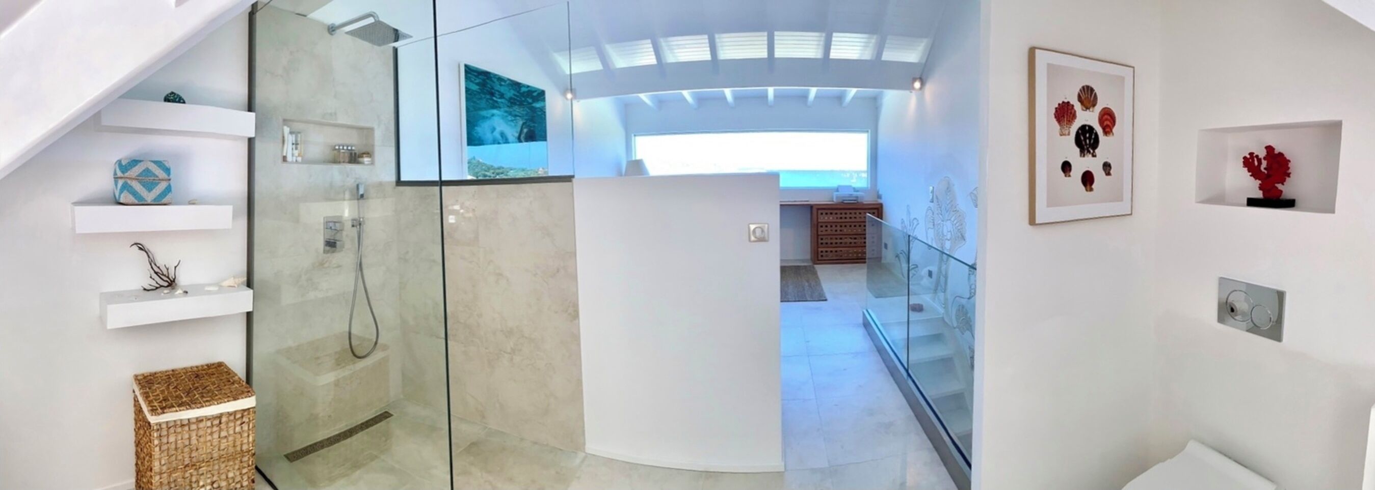 Un baño moderno con cabina de ducha de vidrio, un lavabo blanco y una puerta de vidrio que da a un dormitorio con un ventanal grande.
