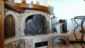 Ein Steinkamin mit einem Metalldrahtgitter, eine Holztür und ein kleines Regal darüber.