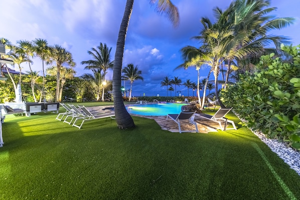 A pool area with artificial grass, lounge chairs, and palm trees.