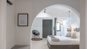 Une chambre à coucher avec un lit, une chaise, un tableau encadré et une porte en arc de cercle.