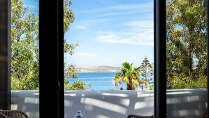 Une vue depuis un balcon, avec une table et des chaises, donnant sur un paysage côtier avec des arbres et un ciel dégagé.