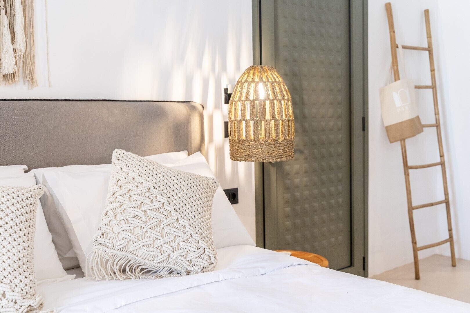 Un dormitorio moderno con cama, almohadones de macramé, una lámpara de fibra y una escalera de madera.
