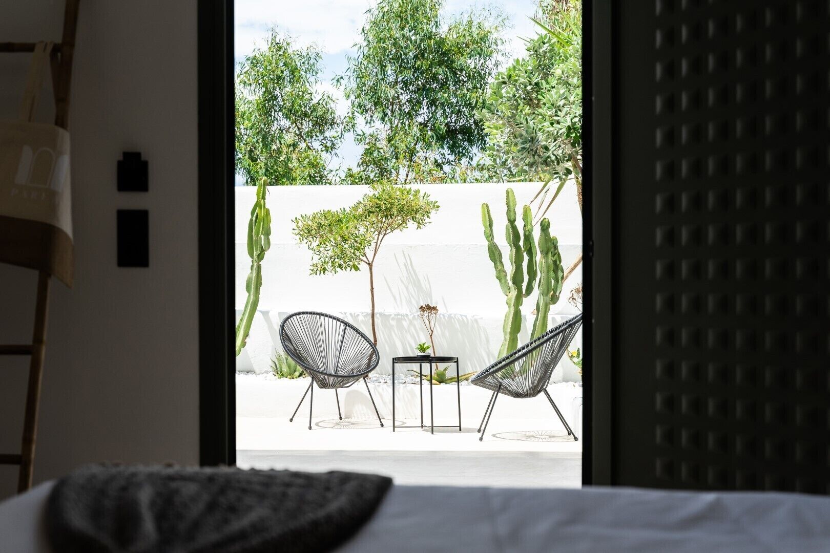 A bedroom with a view of an outdoor patio featuring two chairs, a small table, and cacti.