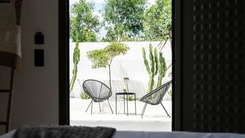 A bedroom with a view of an outdoor patio featuring two chairs, a small table, and cacti.