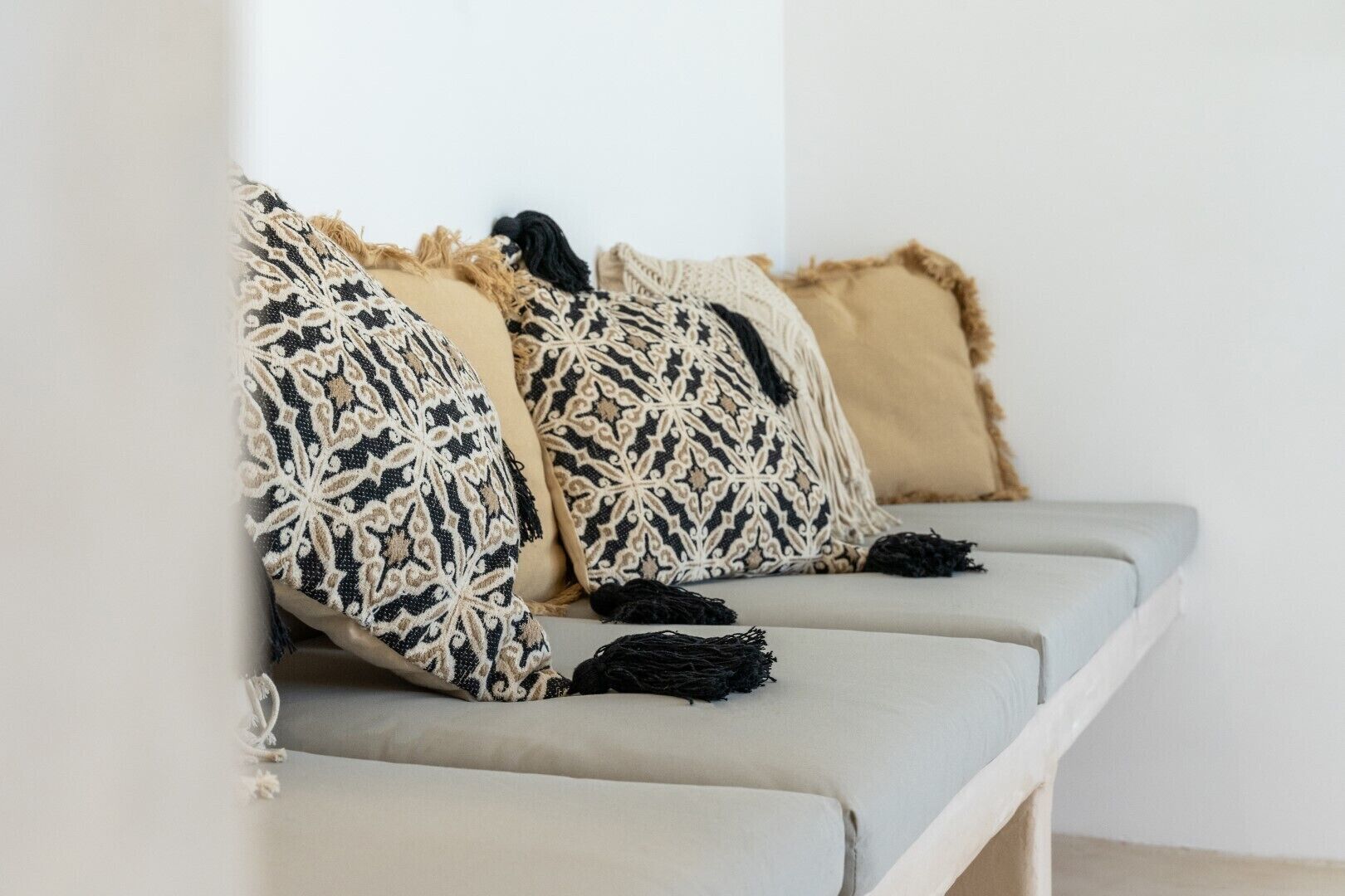 Ein hellgraues Sofa mit drei Kissen in Musteroptik und Fransen.