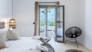 Une chambre d’hôtel moderne avec un lit, une chaise noire et une vue sur la mer, visible à travers une porte vitrée.