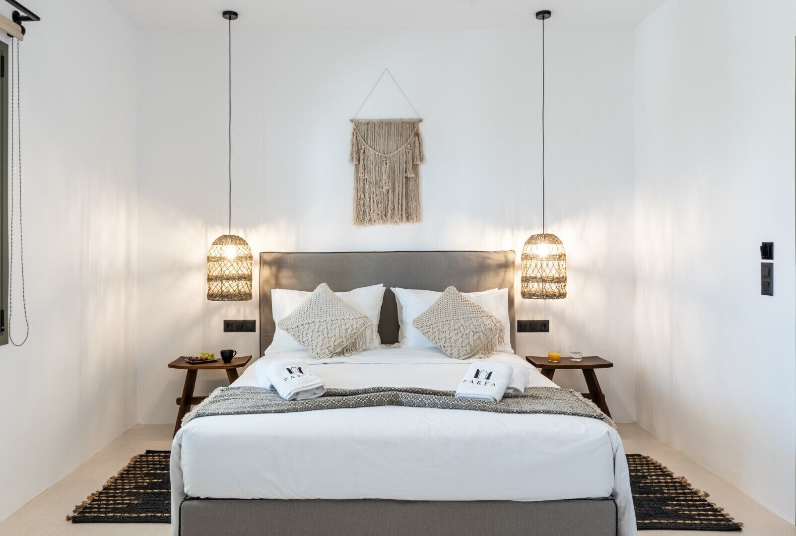 Un dormitorio moderno con una cama grande, dos mesitas de noche y un adorno colgante de macramé sobre la cama.