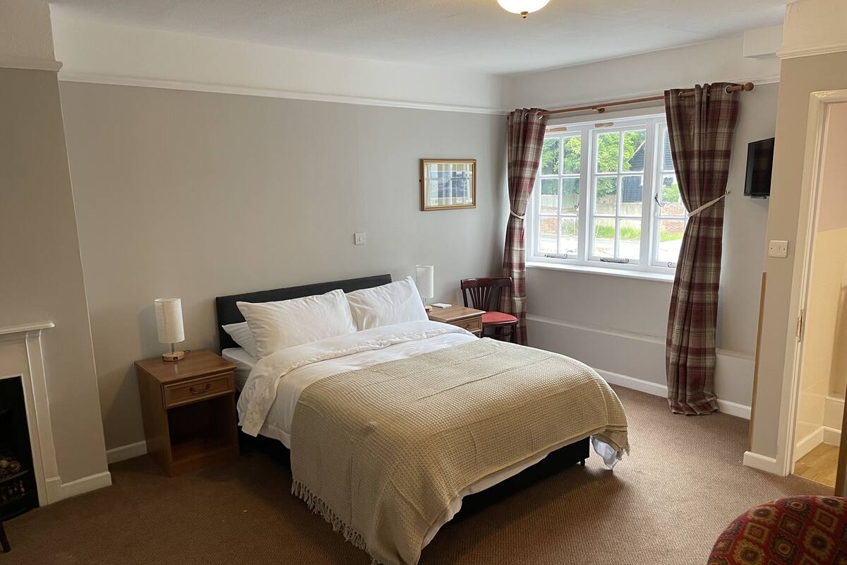 A neatly arranged bedroom with a bed, bedside tables, a chair, and a window with curtains.